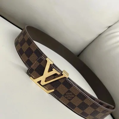 A brown checked-canvas belt with a gold square buckle, laid across a cream sofa cushion