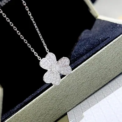 A silver four-leaf-clover pendant on a fine chain, resting on the navy velvet inside its box