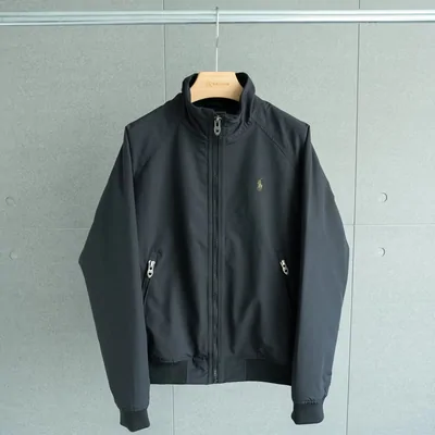 A dark green zip-up jacket with a stand collar, on a hanger against a pale wall