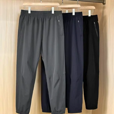 Three pairs of tapered jogger trousers on wooden hangers, grey, navy and black